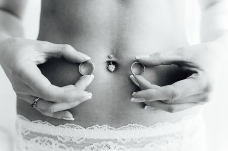 sexy bride in lingerie holds rings near her bellyの写真素材