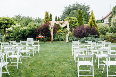 White wedding chairs decorated with fresh flowers on a green grass.の写真素材