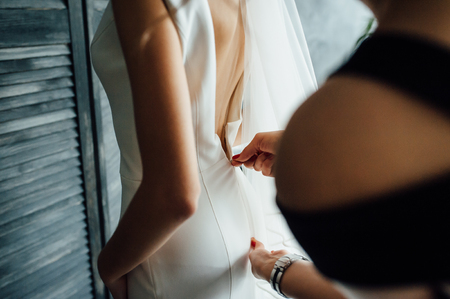 Bridesmaid helps zip up a bride on her dress, preparing bride in morning for the wedding day.の写真素材