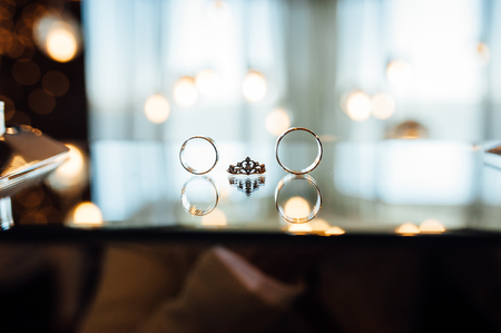 Gold wedding rings lie on the mirror and the light bulbs on the backgroundの写真素材