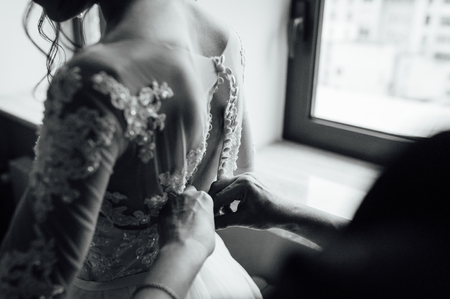 Gorgeous, blonde bride in white luxury dress is getting ready for wedding. Morning preparations. Woman putting on dress.の写真素材