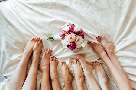 Legs of the bride and bridesmaids, and flower bouquets on the bed. Wedding dayの写真素材