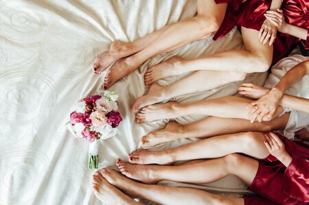 Legs of the bride and bridesmaids, and flower bouquets on the bed. Wedding dayの写真素材