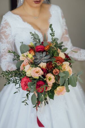 bride in a white dress holding a bouquet of flowers and greeneryの写真素材