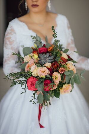 bride in a white dress holding a bouquet of flowers and greeneryの写真素材