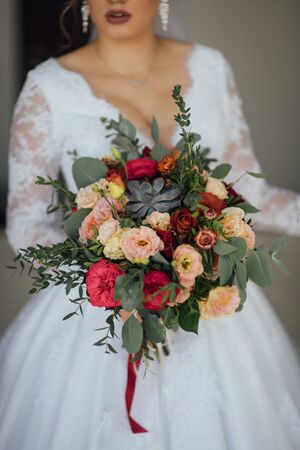 bride in a white dress holding a bouquet of flowers and greeneryの写真素材