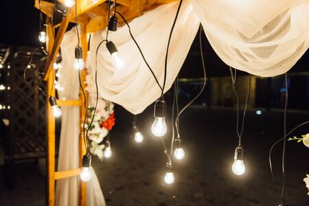 night wedding ceremony. A garland of light bulbs. candles in glass flasks in the evening.の写真素材