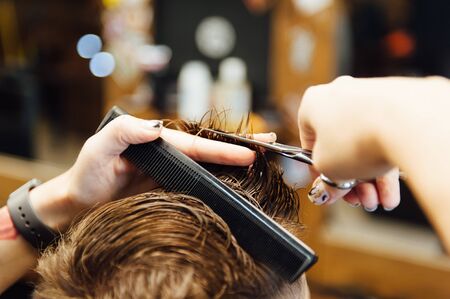 The hands of young barber making haircut to attractive man in barbershopの写真素材