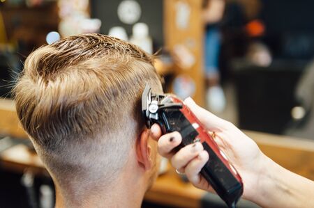 The hands of young barber making haircut to attractive man in barbershopの写真素材