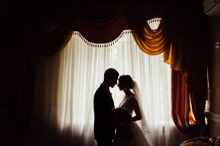 portrait of a romantic couple , silhouette, couple of lovers groom and bride at the window.の写真素材