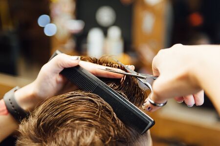 The hands of young barber making haircut to attractive man in barbershopの写真素材