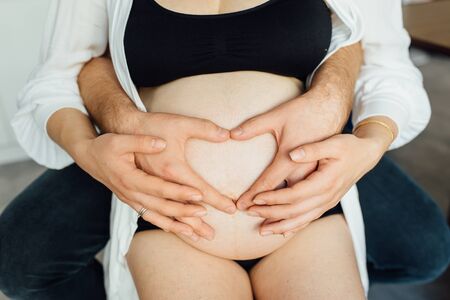 Cropped image of beautiful pregnant woman and her handsome husband hugging the tummyの写真素材