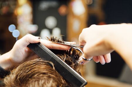 The hands of young barber making haircut to attractive man in barbershopの写真素材