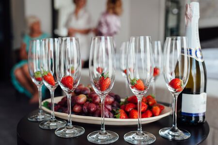 a row of classic glasses with strawberries ready to pour champagne from a bottle. Sparkling wine glasses ready for toastingの写真素材