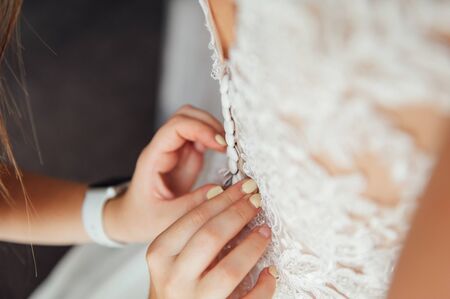 Bridesmaid preparing bride for the wedding day. Bridesmaid helps fasten a wedding dress the bride before the ceremony. Luxury bridal dress close up. Best wedding morning. Wedding conceptの写真素材