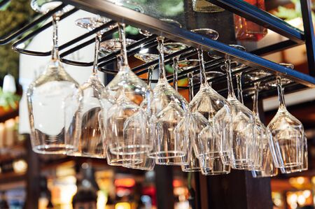 Clean wine glasses hanging upside down above a bar rack in restaurant. Bartender wipes glassesの写真素材