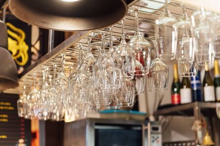 Clean wine glasses hanging upside down above a bar rack in restaurant. Bartender wipes glassesの写真素材