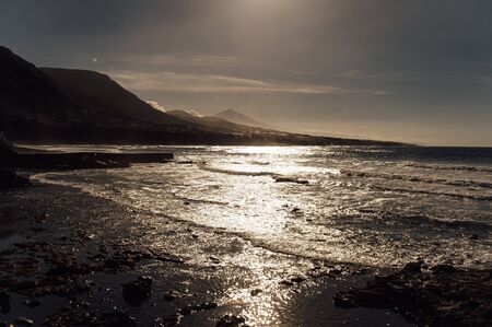 Flight above ocean waves facing beautiful sunset and mountains on horizon.の写真素材
