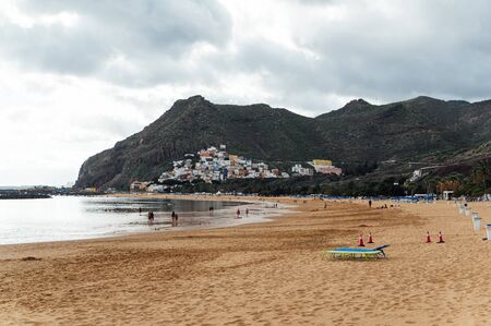 View from the height of the golden sand, palm trees, sun loungers, unrecognizable people on the beach Las Teresitas, Tenerife, Canaries, Spain. cloudy weatherの写真素材