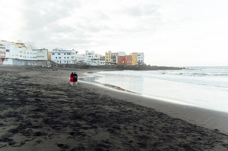 Couple in love walking on the beach near the powerful ocean with the sunset in Puerto de la cruz, Tenerife, Spainの写真素材