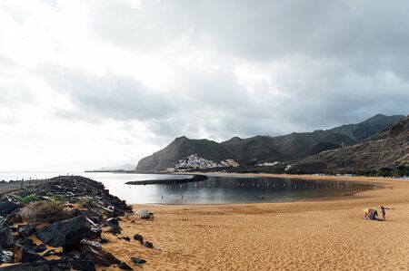 View from the height of the golden sand, palm trees, sun loungers, unrecognizable people on the beach Las Teresitas, Tenerife, Canaries, Spain. cloudy weatherの写真素材