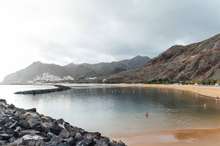 View from the height of the golden sand, palm trees, sun loungers, unrecognizable people on the beach Las Teresitas, Tenerife, Canaries, Spain. cloudy weatherの写真素材
