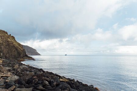 Hills facing the ocean on a sunny day in Tenerife, Canary Islands, and cargo ship waiting outside the portの写真素材