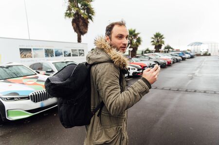 A tourist with a heavy backpack in the parking lot is looking for a car rental companyの写真素材