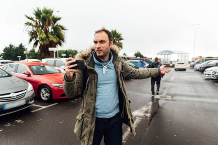 A tourist with a heavy backpack in the parking lot is looking for a car rental companyの写真素材
