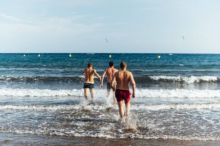 Three Caucasian friends running at sea with splash for swimming in sunset background. Tenerife islandの写真素材
