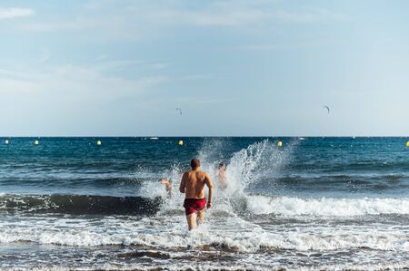 Three Caucasian friends running at sea with splash for swimming in sunset backgroundの写真素材