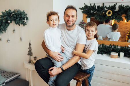 happy father hugs his sons. Photo taken in an apartment with a Christmas treeの写真素材