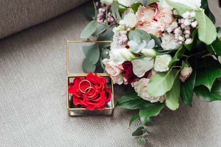 on the glass table in the room is a box with wedding rings, next to it is a bouquet of flowers