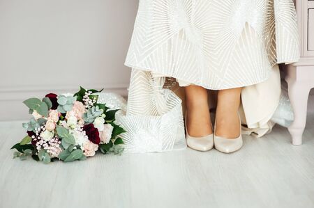 Wedding shoes of the bride with a bouquet of peonies and other flowers.の写真素材