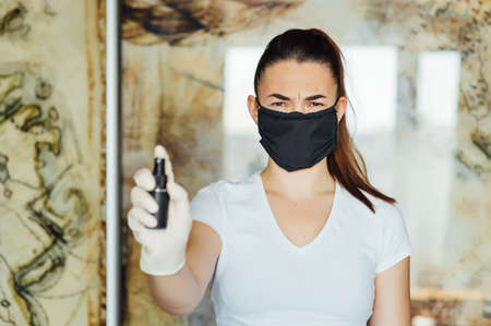 A girl in a protective mask, glasses and gloves spray an antiseptic to prevent infection.の写真素材