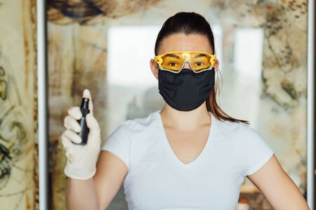 A girl in a protective mask, glasses and gloves spray an antiseptic to prevent infection.の写真素材