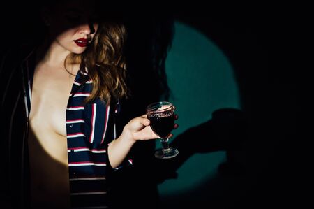girl on green background with a glass of red drink wine smoke looks asideの写真素材