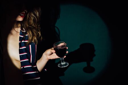 girl on green background with a glass of red drink wine smoke looks asideの写真素材