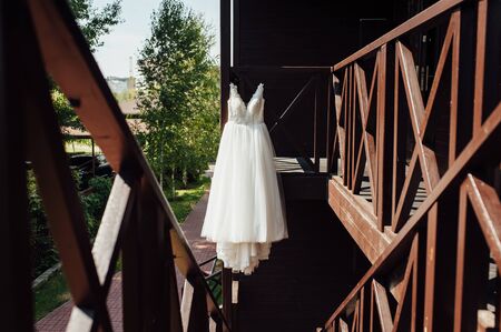 Elegant wedding dress hanging on a wooden railing outsideの写真素材