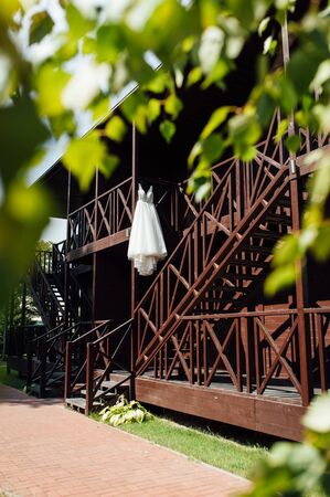 Elegant wedding dress hanging on a wooden railing outsideの写真素材