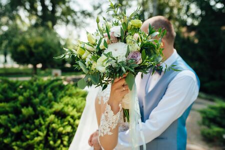 Cheerful newlyweds are hugging at their wedding and covering their face with a wedding bouquetの写真素材