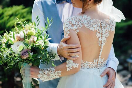 Cheerful newlyweds are hugging at their wedding and covering their face with a wedding bouquetの写真素材