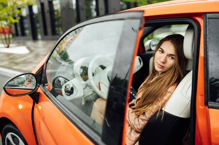 Gorgeous girl with long hair sitting in a red electric carの写真素材