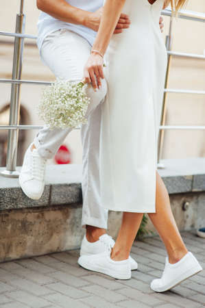 A loving couple in white clothes and sneakers hugs with their handsの写真素材