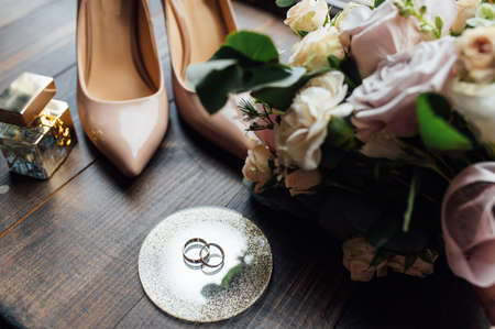 beautiful gold wedding rings on wood floor next to bouquet and shoesの写真素材