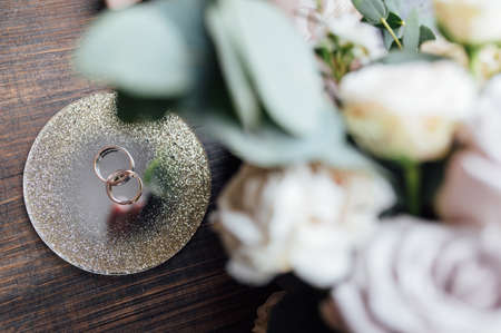 beautiful gold wedding rings on wood floor next to bouquet and shoesの写真素材