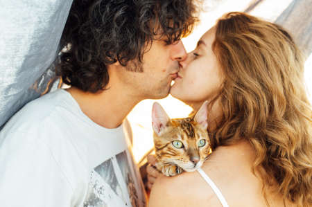 A happy girl with a cat in her arms gently kisses her boyfriend.の写真素材