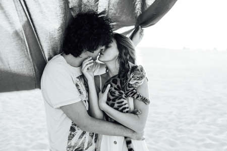 A happy girl with a cat in her arms gently kisses her boyfriend.の写真素材