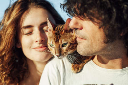 Cheerful young couple having fun on the beach with their bengal catの写真素材