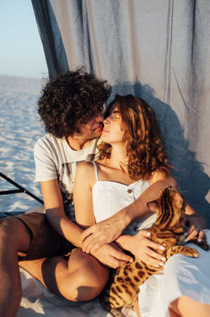 Romantic couple hugging with a cat on the beach. In the background is a gray clothの写真素材